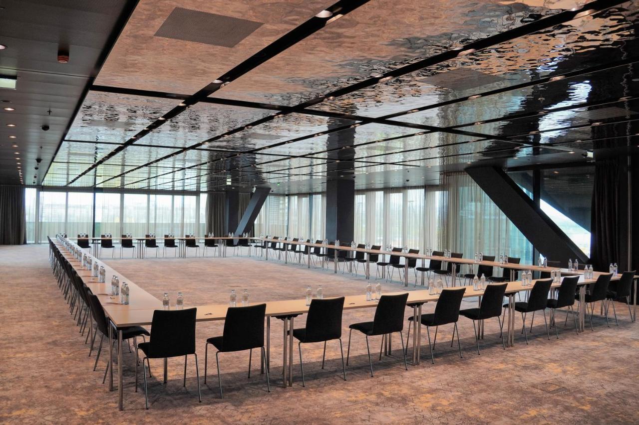 Melia Vienna Hotel Exterior foto The photo shows a modern conference room with a long rectangular table arranged in a U-shape. The table is flanked by multiple black chairs. The room features a sleek, reflective ceiling that gives a contemporary feel, and large windows allow natural