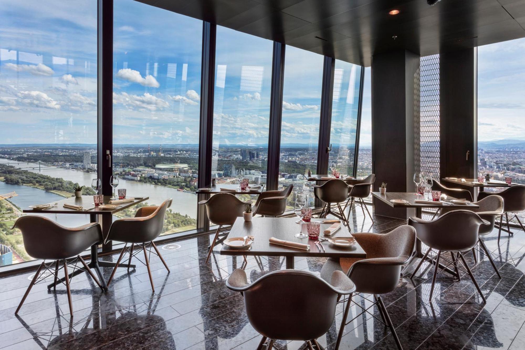 Melia Vienna Hotel Exterior foto The photo shows a modern dining space with a sleek design, featuring several tables and chairs arranged near large floor-to-ceiling windows. These windows provide a panoramic view of a river and surrounding landscape. The dining area has a contempora