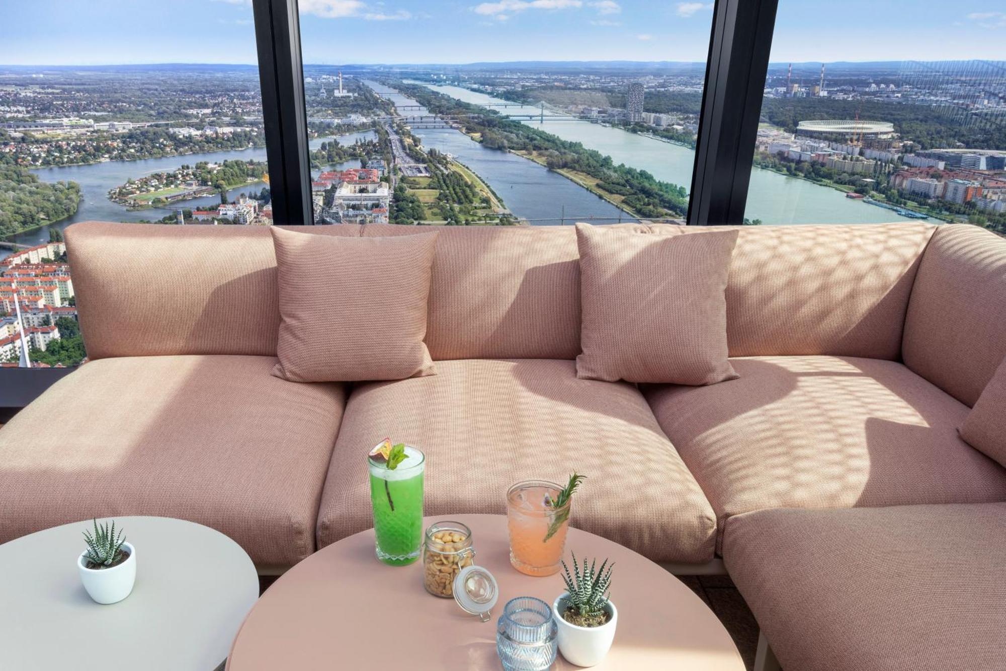 Melia Vienna Hotel Exterior foto The photo shows a cozy seating area with a large, soft, light pink couch and some small decorative pillows. In front of the couch, there is a round table with a few drinks placed on it: a green cocktail with a garnish, a light pink drink, and some sn