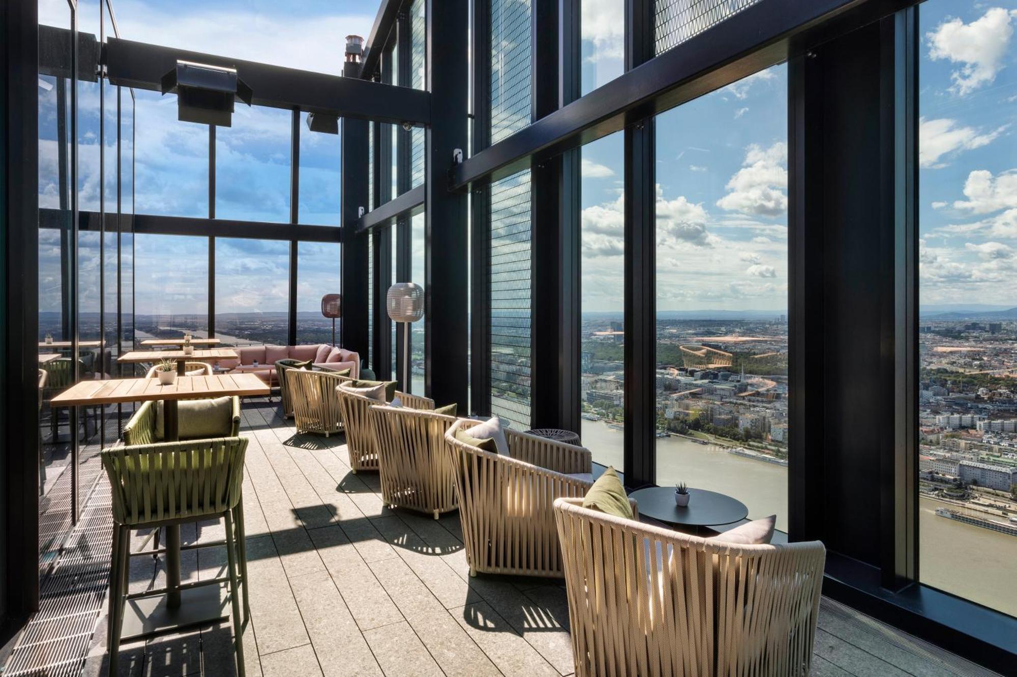 Melia Vienna Hotel Exterior foto The image shows a stylish indoor space with large floor-to-ceiling windows that provide a panoramic view of the landscape outside. The area features several comfortable seating arrangements, including modern chairs and small tables. The design is sle