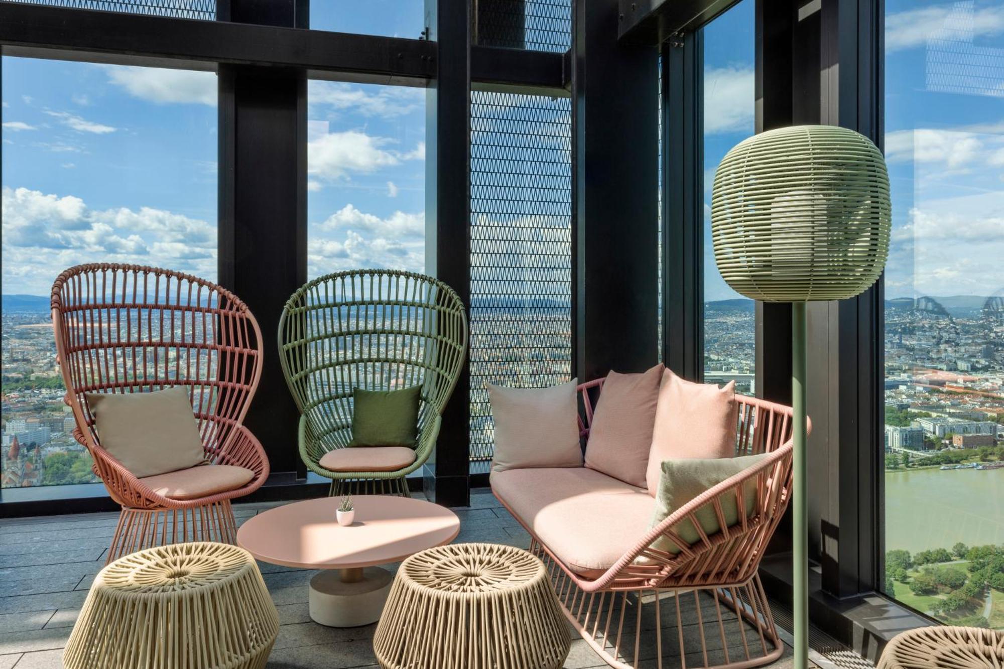Melia Vienna Hotel Exterior foto The photo shows a modern lounge area with large windows offering a view of the outdoors. There are two stylish, high-backed chairs made of wicker in pastel colors—one pink and one green. A cozy sofa in a soft pink hue is positioned between them, acco